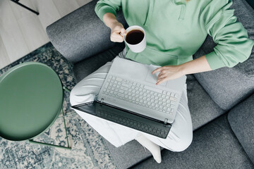 Woman working at home using laptop and drinking coffee, top view close-up
