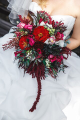 the bride in a white slinky dress holds a wedding bouquet of red flowers of zinnias