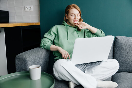 young redhead caucasian woman wearing a green hoodie at home shopping online using laptop