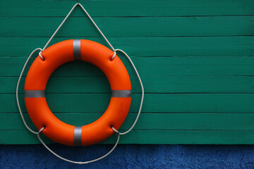 Orange lifebuoy hanging on green wooden board, space for text. Rescue equipment