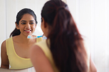 Reflection of a young woman standing in front of mirror with holding toothbrush