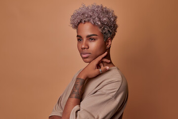 Young attractive blonde African American woman millennial shows tattoo on arm and touches chin with...