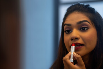 Close-up portrait of young woman applying red lipstick 