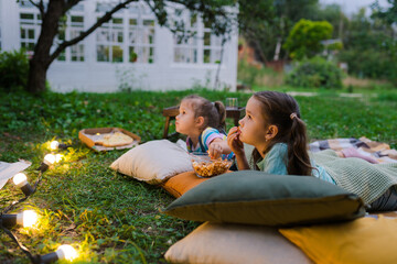 Children lying on plaid and looking movie on backyard. Summer outdoor weekend activities with kids. Open air cinema. Backyard movie night with popcorn