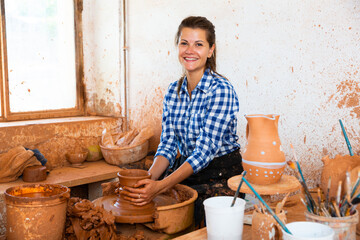 Female artisan in ceramics workshop with pottery wheel and various clay vessels. High quality photo