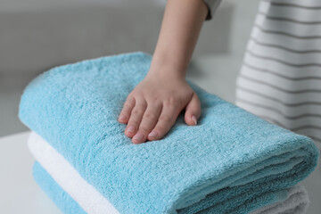 Woman touching soft light blue towel indoors, closeup