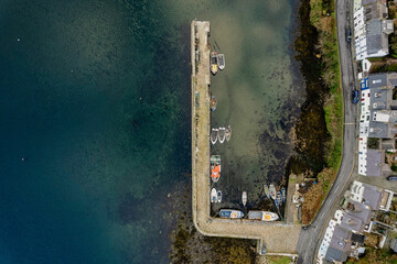 Ocean surface and a pier and fishing boats and waterfront houses by a road. Top down aerial view....
