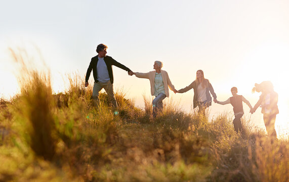 Grandpa is in the lead. Shot of a multi-generational family walking hand in hand across a field at sunset.