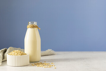 Barley milk in a glass bottle tied with canvas thread. Barley grains in a white vase on a light...