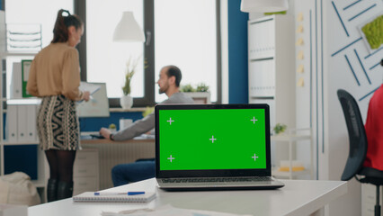 Close up of laptop with green screen on empty desk in business office. Mock up template with...