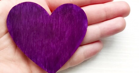 Hand holds a purple heart. Expression of understanding and compassionate love. Love and caring. The...