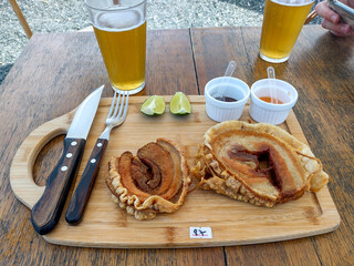 Meal of roast pork, with lemon, special sauces, served with beer, table and rustic table, with cutlery. 