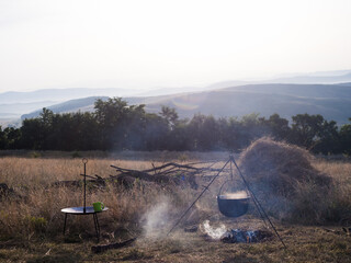 Cooking breakfast on fire in mountains. Camping season. Cauldron morning sunrise view