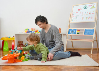 Father and sweet little child boy having fun playing with cars and colorful toys, on the floor, at home. Beautiful family moment, indoors