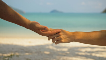 Hands of flirting young man and woman touching on beach in palms shadow against calm azure ocean close view. Traveling to tropical countries