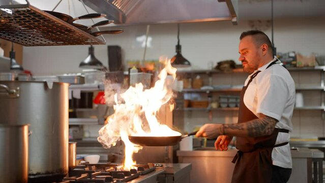 Professional chef preparing meal, flambing indoors in restaurant kitchen.