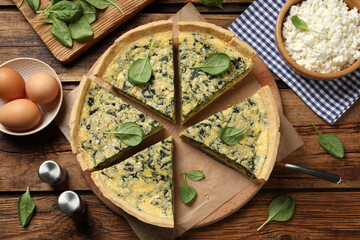 Cut delicious spinach pie with ingredients on wooden table, flat lay