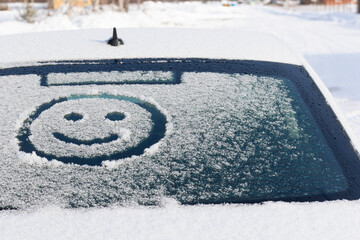 Drawing of a smiling face on a snowy rear window of a car on a winter sunny day. Selective focus. Close-up