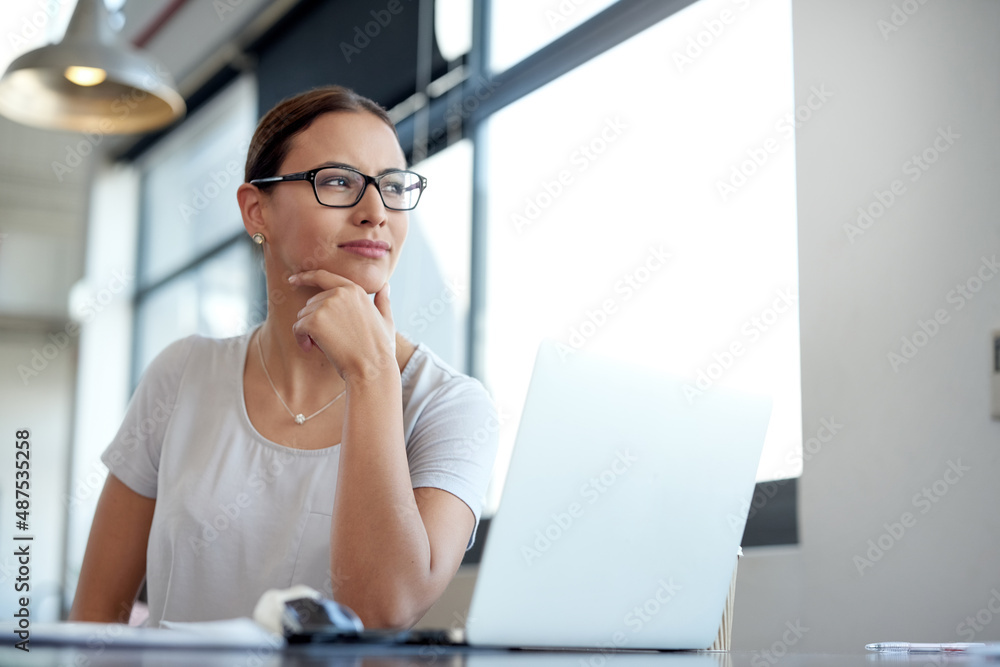 Poster dreaming up new ideas. shot of a young woman looking through a window while working on a laptop in a