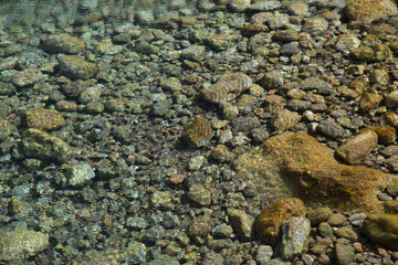 Ripples and sunlight reflexes in a large rock pool filled with pebbles