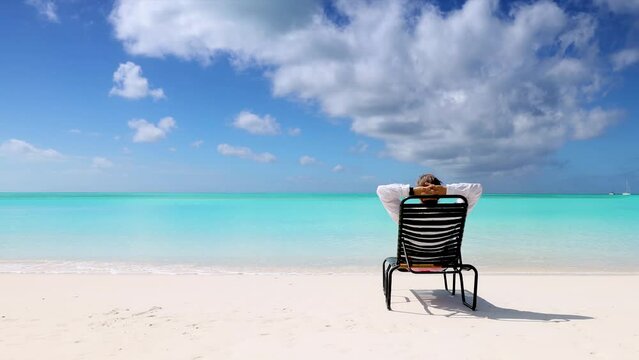 A man relaxes in a chair on a tropical paradise beach in the Caribbean with turquoise sea and blue sky during his vacation time