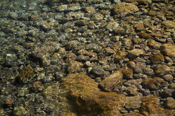 Ripples and sunlight reflexes in a large rock pool filled with pebbles
