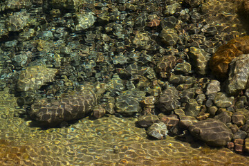 Ripples and sunlight reflexes in a large rock pool filled with pebbles