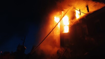 The roof of the house is on fire. The residential building burn, village. Firefighters put out a fire from the crane from above. The fire Department putting out the open flame. Smoke and sparks.