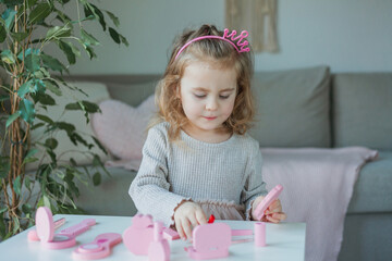 Cute little girl is playing in beauty salon with children's cosmetics at home.