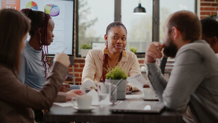 Close up of company worker planning business strategy with colleagues, using analysis documents in boardroom. Woman having conversation with coworkers at startup company meeting.