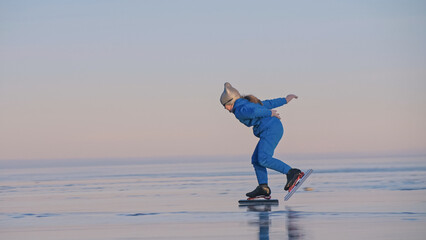 The girl train on ice speed skating. The child skates in the winter in blue sportswear suit, sport glasses. Children speed skating sport. Outdoor slow motion. Snow capped mountains, beautiful ice.