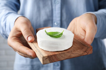 Woman holding serving board with delicious brie cheese on blurred background, closeup