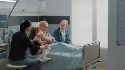 Child hugging sick grandpa in hospital ward bed at visit, comforting aged patient with illness. Kid...