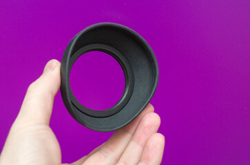 Man's hand holding a rubber hood for a photo lens on a purple background