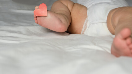 Children's heels, baby, lie on the bed under the blanket with a tag on the finger, with a heart. Valentine's Day.