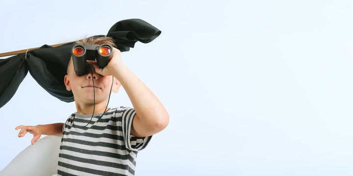 Little child boy playing with cardboard ship on blue wall background