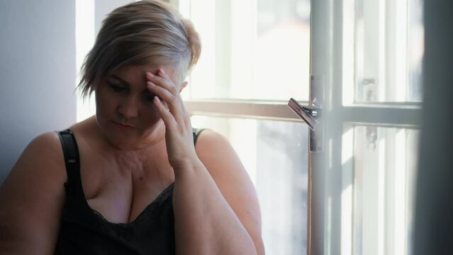 Depressed lonely fat woman sitting aby window at home and thinking.