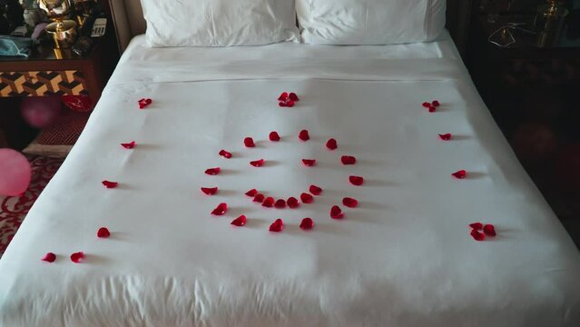 Emoticon from red rose petals on the bed. White linens in an expensive hotel. Romantic evening. Service in the hotel business. Honeymoon room