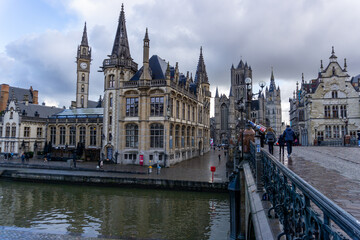 Fototapeta premium Panoramic of Ghent next to the water channels, from the bridge, with a view of the Ghent church on a cloudy and gray day.