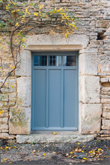 Une porte bleue fermée avec un mur en pierres. Un roncier et une porte bleue.