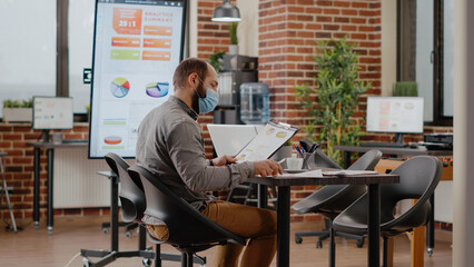 Business man with face mask greeting colleagues in boardroom, meeting to work on marketing presentation and project during pandemic. Employee working with people to plan strategy.