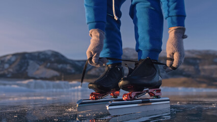 The child train on ice speed skating. Athlete puts on skates. The girl skates in the winter in sportswear, sport glasses. Children speed skating short long track, kid sport. Outdoor slow motion.