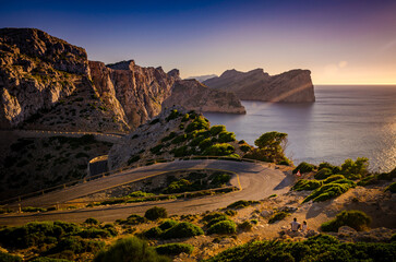 Serpentine at sunset with the couple sitting beside the road. Lighthouse of Cap de Formentor (Spain)