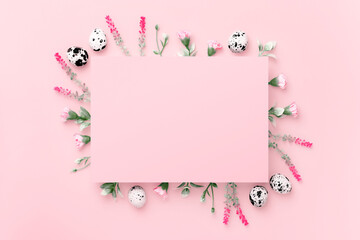 Easter composition. Easter eggs, flowers, paper blank on pastel pink background. Flat lay, top view, copy space.