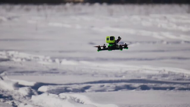 A quadcopter with a camera flies over the snow cover in the field. The camera follows the drone