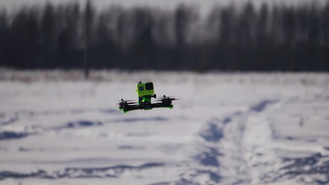 Cool close-up of a drone flying with a camera across a snowy winter field. The camera follows the drone