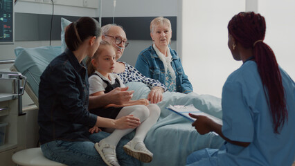 Healthcare specialist doing check up visit with patient and his family in hospital ward. Medical...