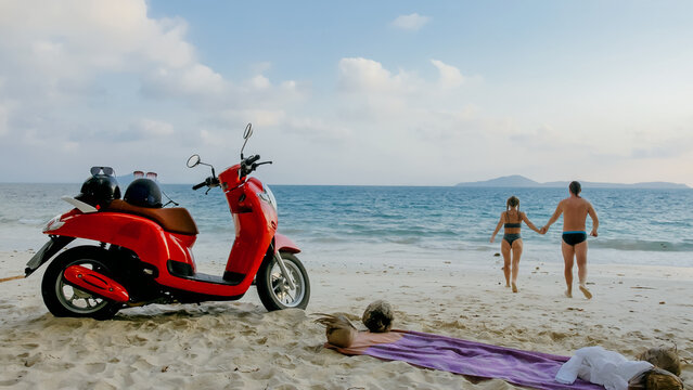 Scooter road trip. Lovely couple on red motorbike in white clothes on sand beach. Wedding just married people walking near tropical palm tree, sea. Honeymoon by ocean. Asia Thailand. Motorcycle rent.