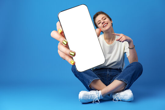 Happy woman shows blank smartphone screen against blue background Stock  Photo | Adobe Stock