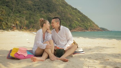 The cheerful love couple holding and eating slices of watermelon on tropical sand beach sea. Romantic lovers two people caucasian spend summer weekend in outdoor. Hat, backpack white shirt beachwear.